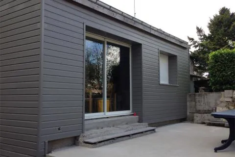 Bardage anthracite sur une extension avec baie vitrée donnant sur une terrasse