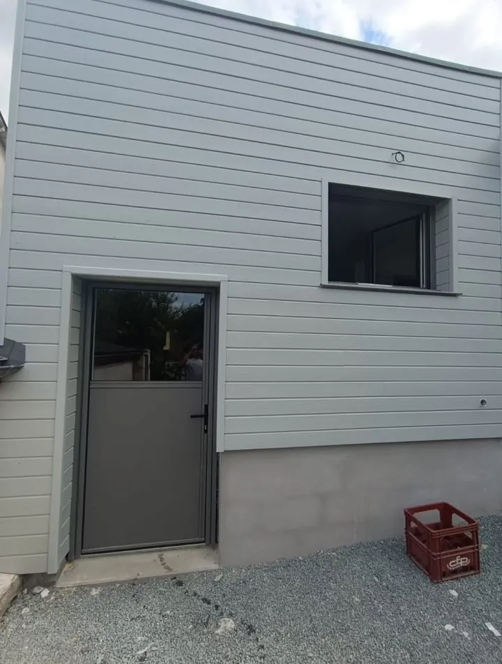Bardage PVC gris posé sur une façade avec porte et fenêtre aluminium