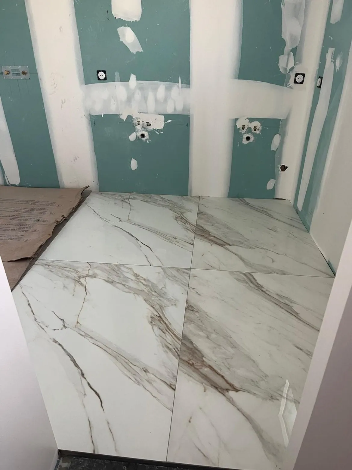 Carrelage grand format effet marbre blanc dans une douche à l'italienne en cours de pose