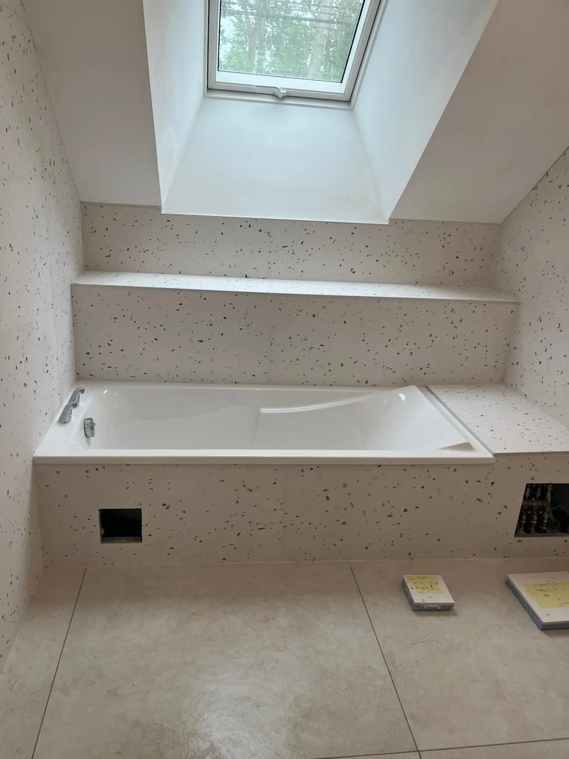 Salle de bain carrelée en terrazzo avec baignoire et banquette sous velux